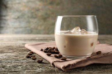 Coffee cream liqueur in glass and beans on wooden table, closeup