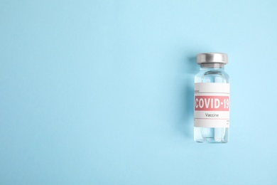 Photo of Vial with coronavirus vaccine on light blue background, top view. Space for text