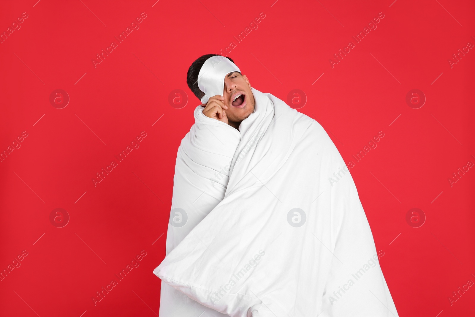 Photo of Man wrapped in blanket yawning on red background