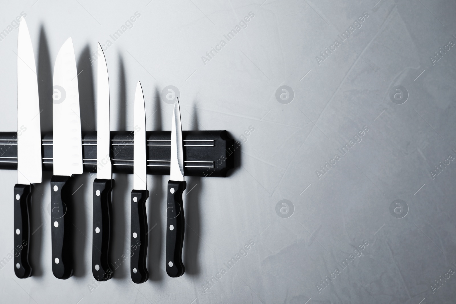 Photo of Magnetic holder with set of knives on grey stone background. Space for text