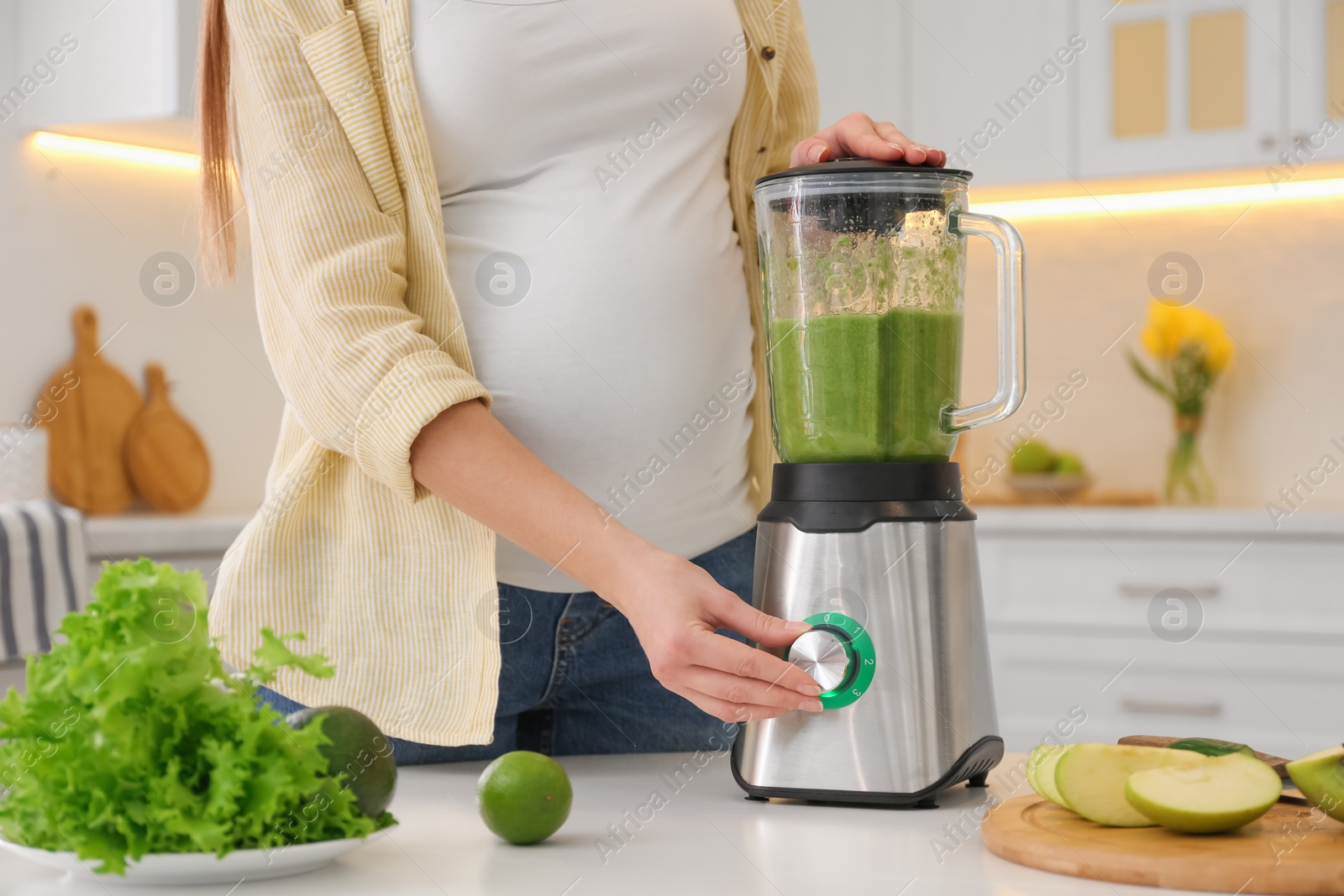 Photo of Young pregnant woman preparing smoothie at table in kitchen, closeup. Healthy eating