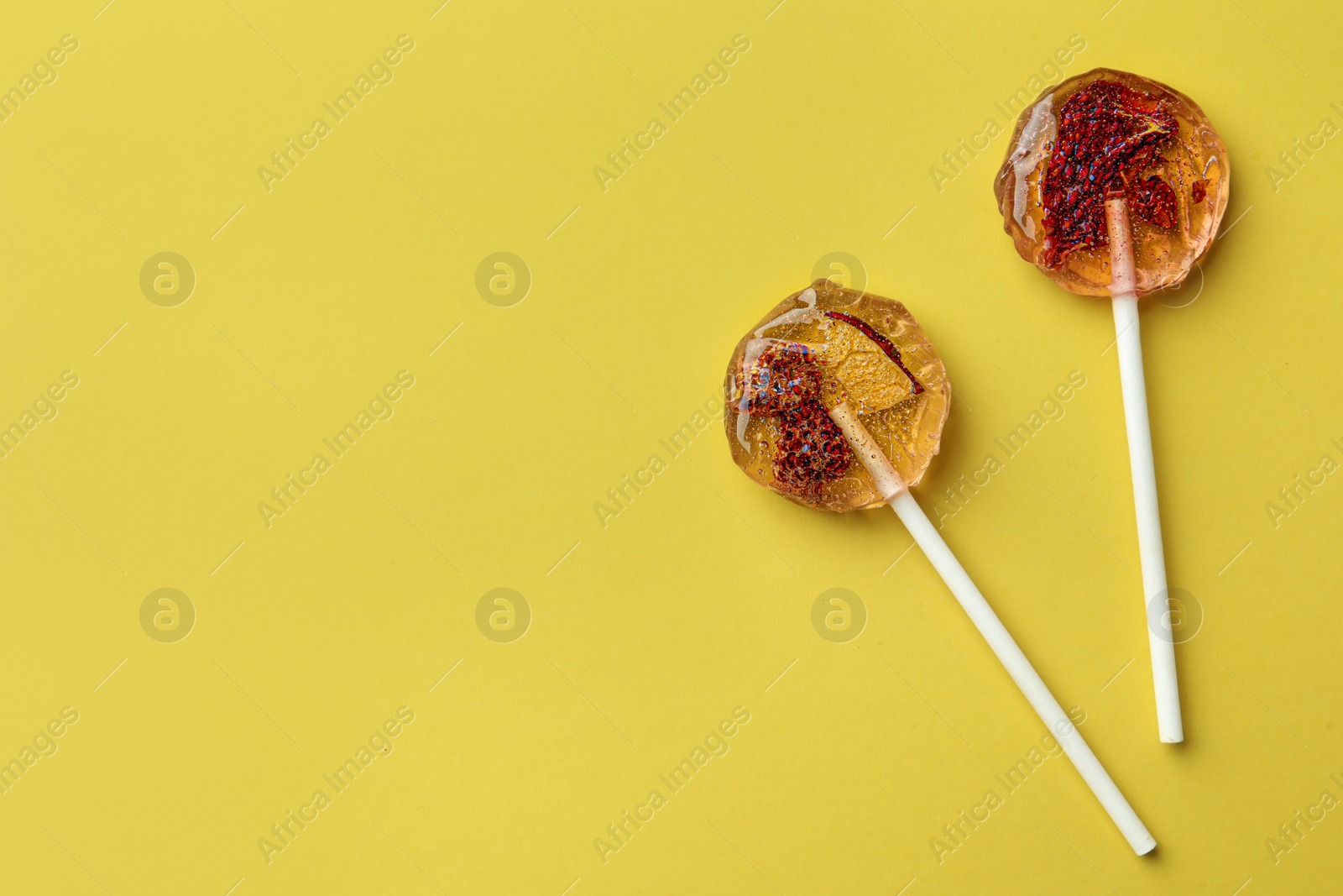 Photo of Sweet colorful lollipops with berries on yellow background, flat lay. Space for text