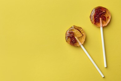 Photo of Sweet colorful lollipops with berries on yellow background, flat lay. Space for text