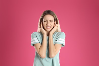 Photo of Emotional young woman covering her ears on pink background