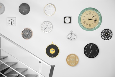 Photo of Many different clocks hanging on white wall. Time of day