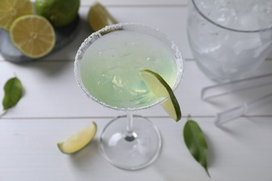 Delicious Margarita cocktail in glass and limes on white wooden table, above view