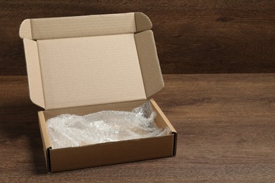 Photo of One open cardboard box with bubble wrap on wooden table. Space for text