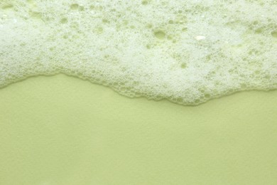 Photo of Fluffy bath foam on light green background, top view. Space for text