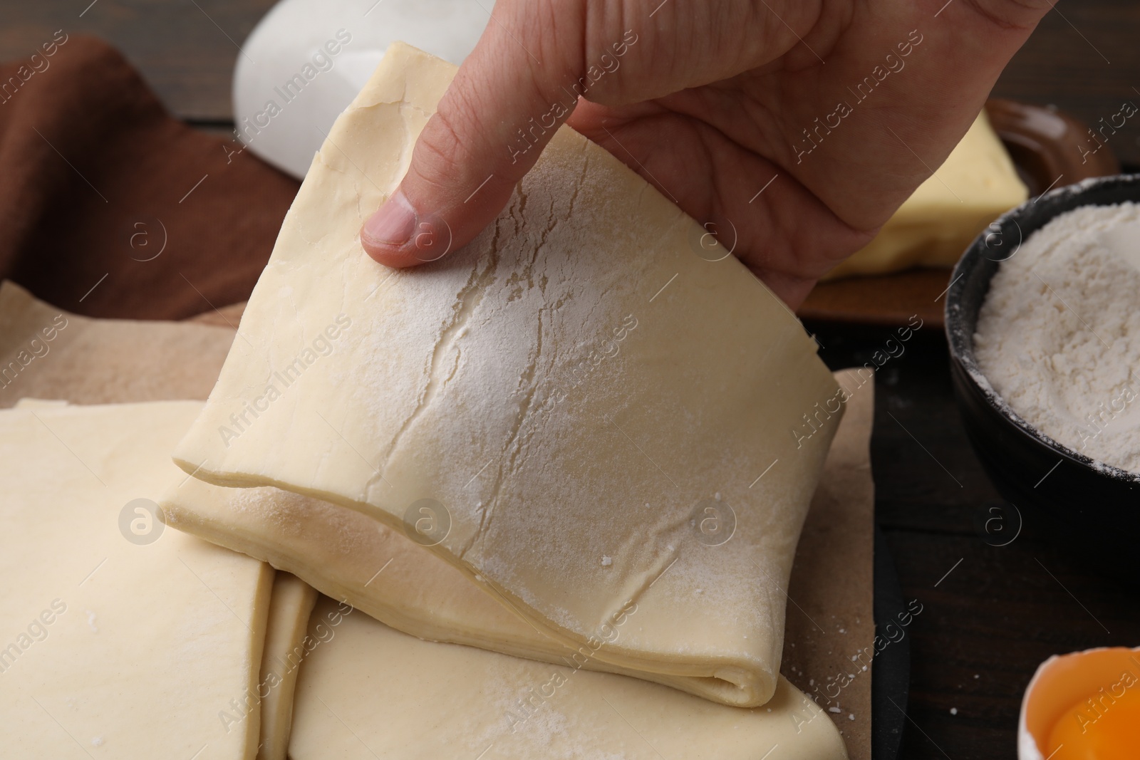 Photo of Man holding raw puff pastry dough at wooden table, closeup