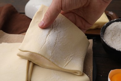 Photo of Man holding raw puff pastry dough at wooden table, closeup