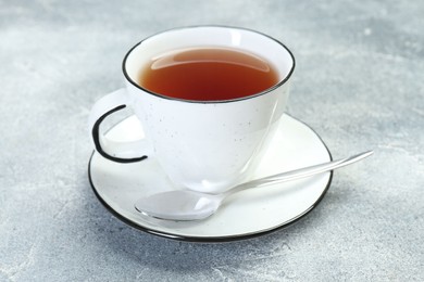 Photo of Aromatic tea in cup and spoon on grey table