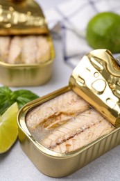 Open tin cans with mackerel fillets on grey table, closeup