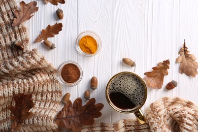 Cup of hot drink, spices, leaves and knitted scarf on white wooden table, flat lay. Cozy autumn atmosphere