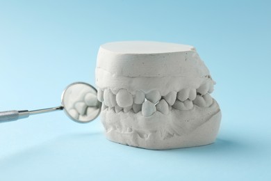 Photo of Dental model with gums and dentist mirror on light blue background. Cast of teeth