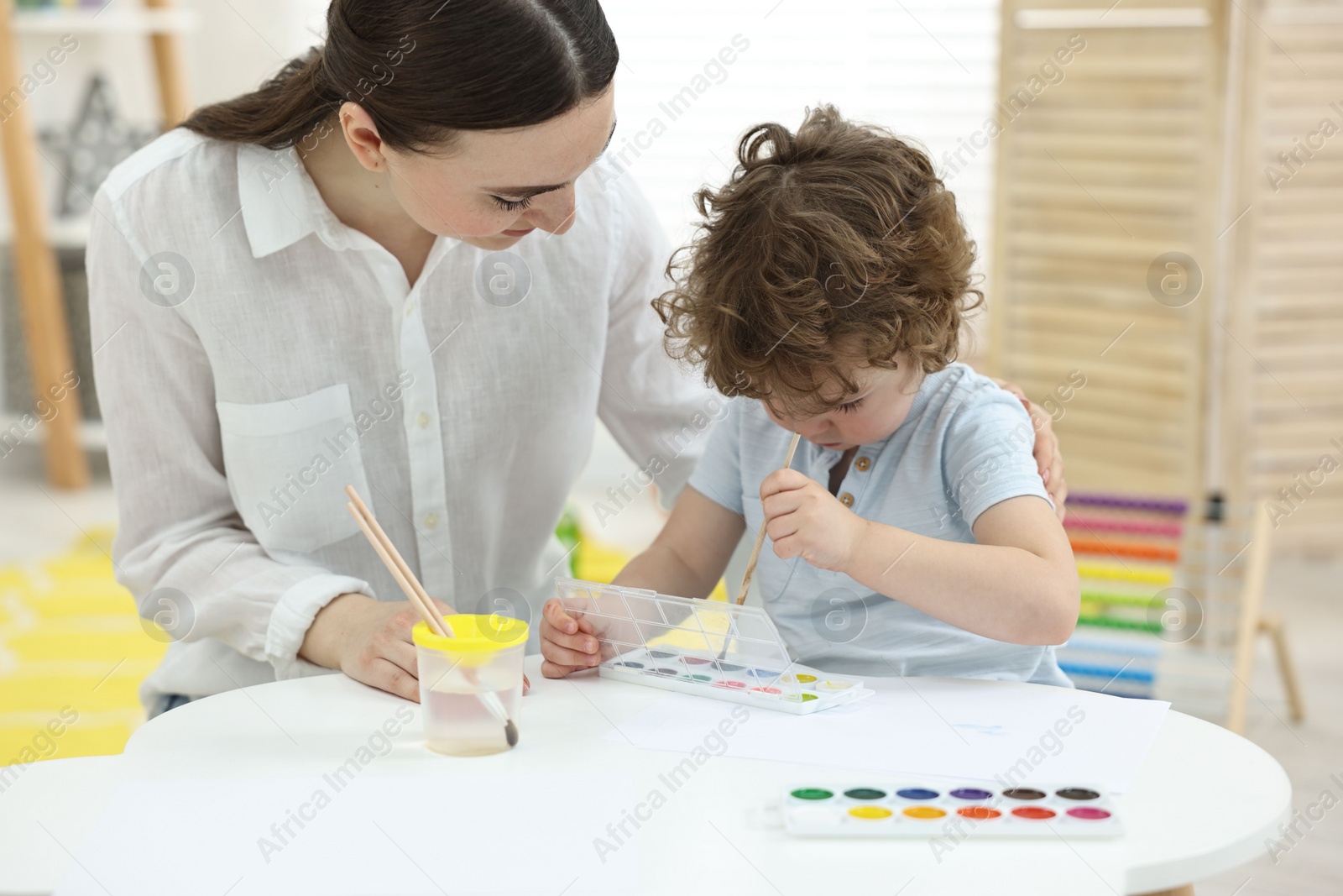 Photo of Mother and her little son painting with watercolor at home
