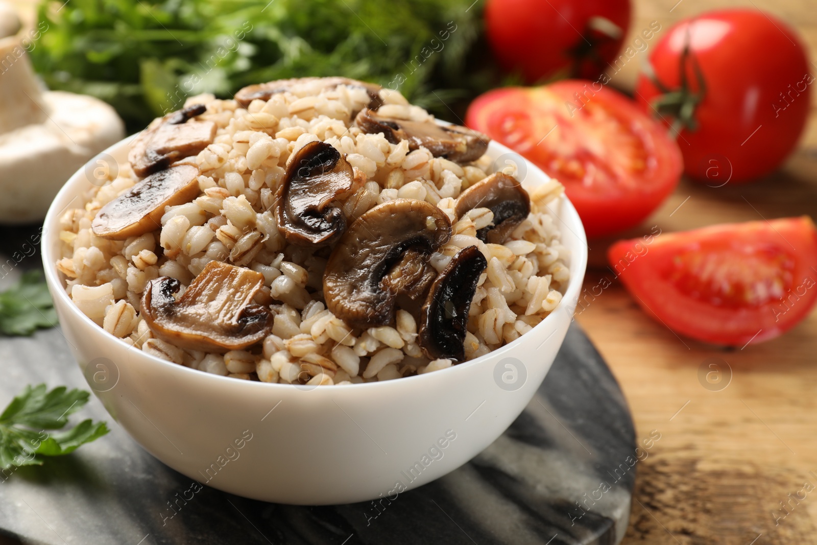 Photo of Delicious pearl barley with mushrooms in bowl served on table, closeup