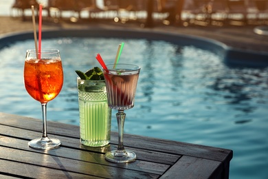 Photo of Glasses of fresh summer cocktails on wooden table near swimming pool outdoors. Space for text