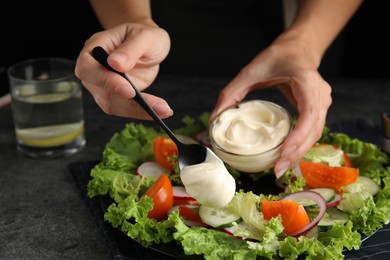 Photo of Woman dressing delicious vegetable salad with mayonnaise at grey table, closeup