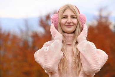 Photo of Young beautiful woman wearing warm earmuffs outdoors