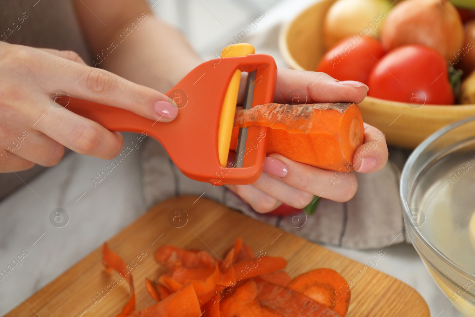 Photo of Woman peeling fresh carrot at white marble table, closeup