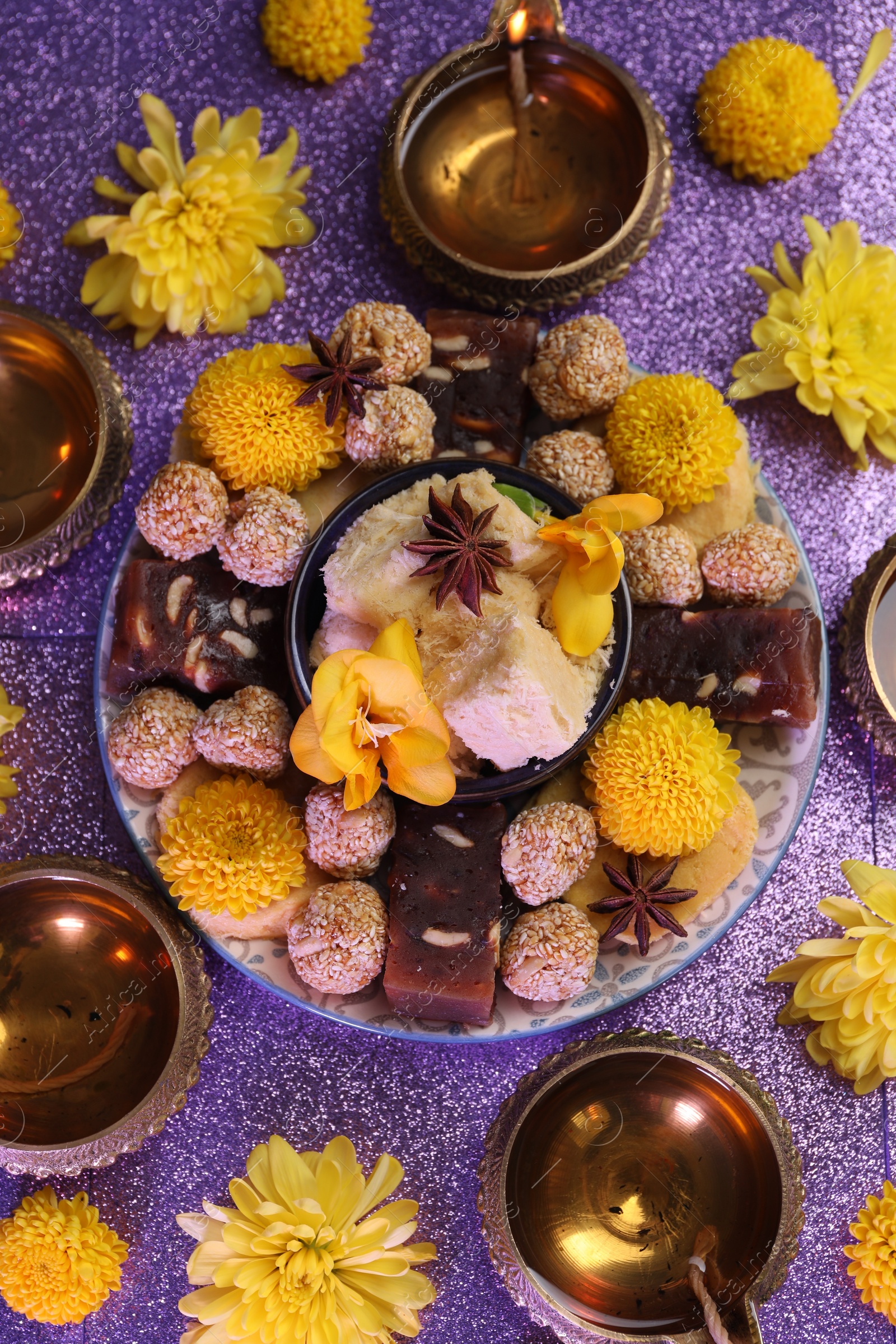 Photo of Diwali celebration. Flat lay composition with diya lamps and tasty Indian sweets on shiny violet table