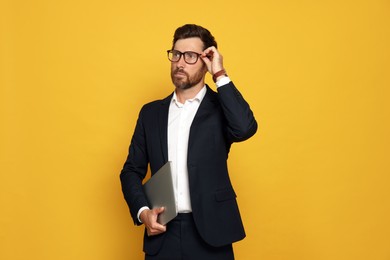 Photo of Portrait of bearded man with glasses and laptop on orange background