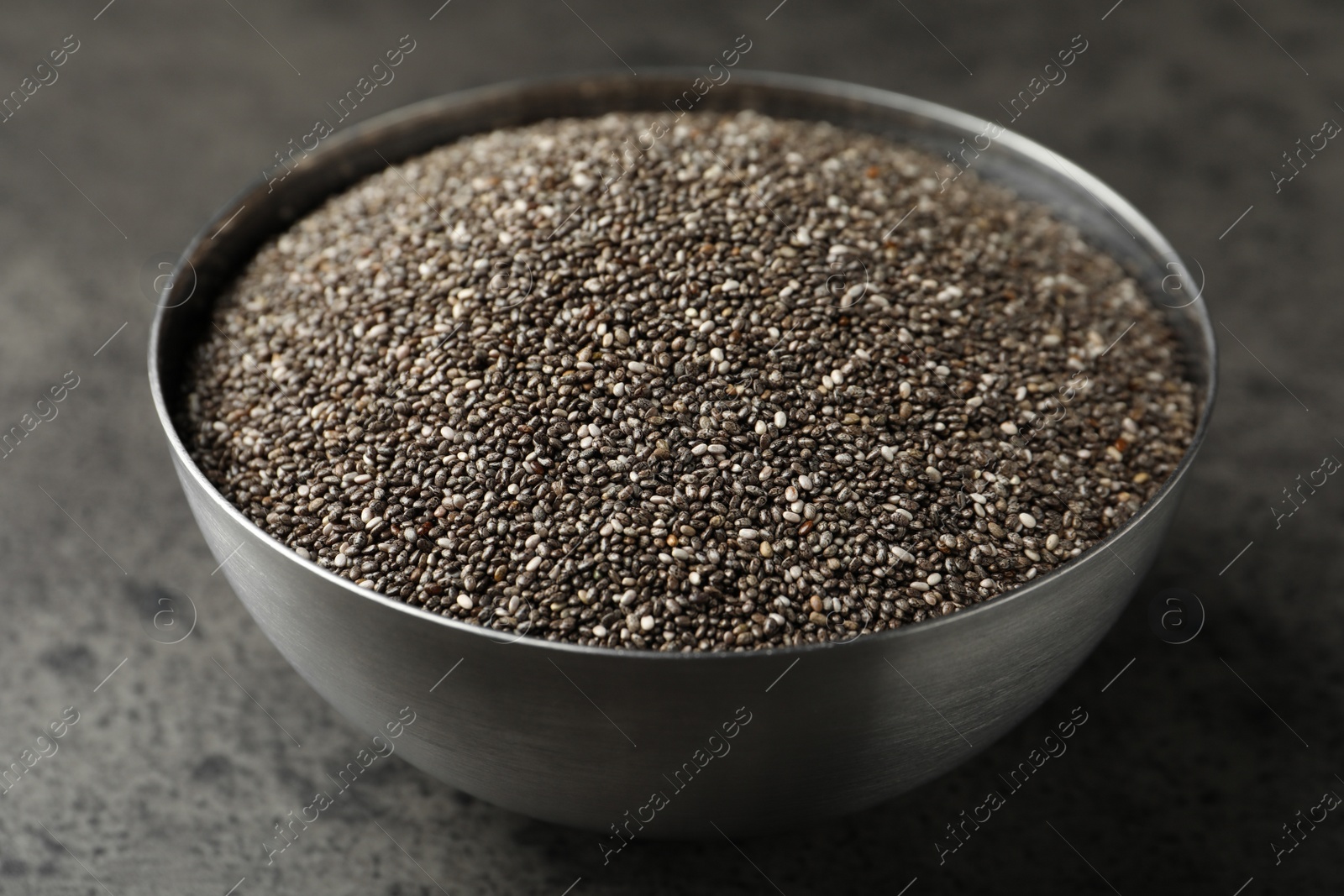 Photo of Metal bowl with chia seeds on grey table, closeup