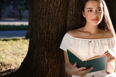 Photo of Beautiful young woman reading book near tree in park