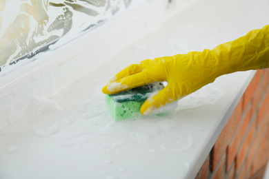 Photo of Woman cleaning window sill with sponge, closeup