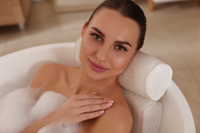 Photo of Young woman using pillow while enjoying bubble bath indoors