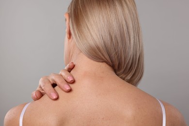 Photo of Woman suffering from pain in her neck on grey background, back view