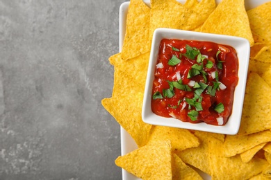 Photo of Plate with delicious mexican nachos chips and salsa sauce on grey table, top view. Space for text