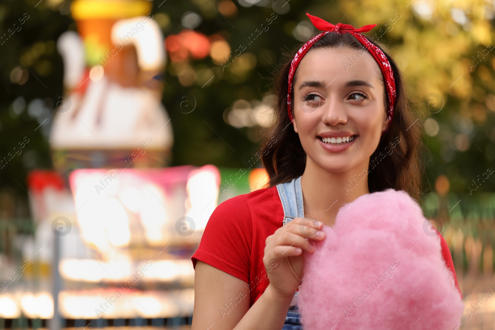 Photo of Stylish young woman with cotton candy at funfair, space for text