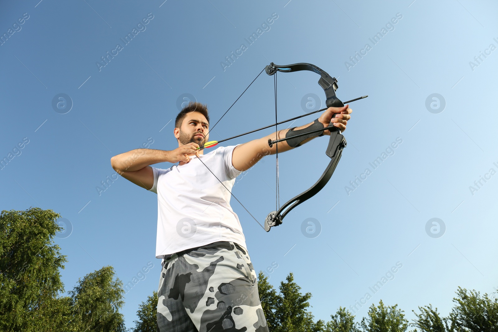 Photo of Man with bow and arrow practicing archery outdoors, low angle view