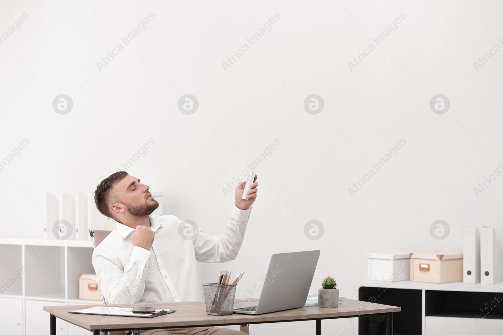 Photo of Young man suffering from heat in office. Air conditioner malfunction