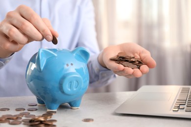 Man putting coin into piggy bank at table indoors, closeup