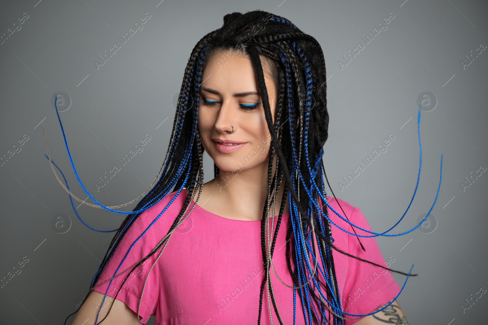 Photo of Beautiful young woman with nose piercing and dreadlocks on grey background