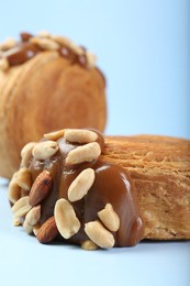 Photo of Supreme croissants with chocolate paste and nuts on light blue background, closeup. Tasty puff pastry