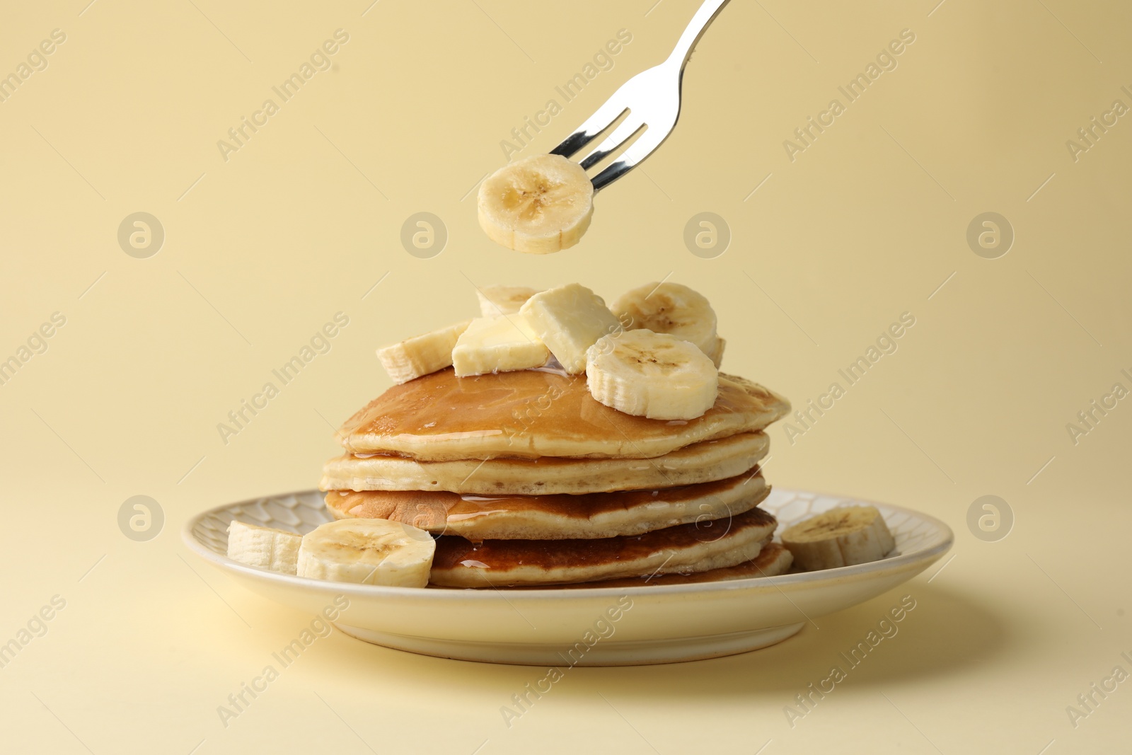 Photo of Eating delicious pancakes with bananas, butter and honey on beige background