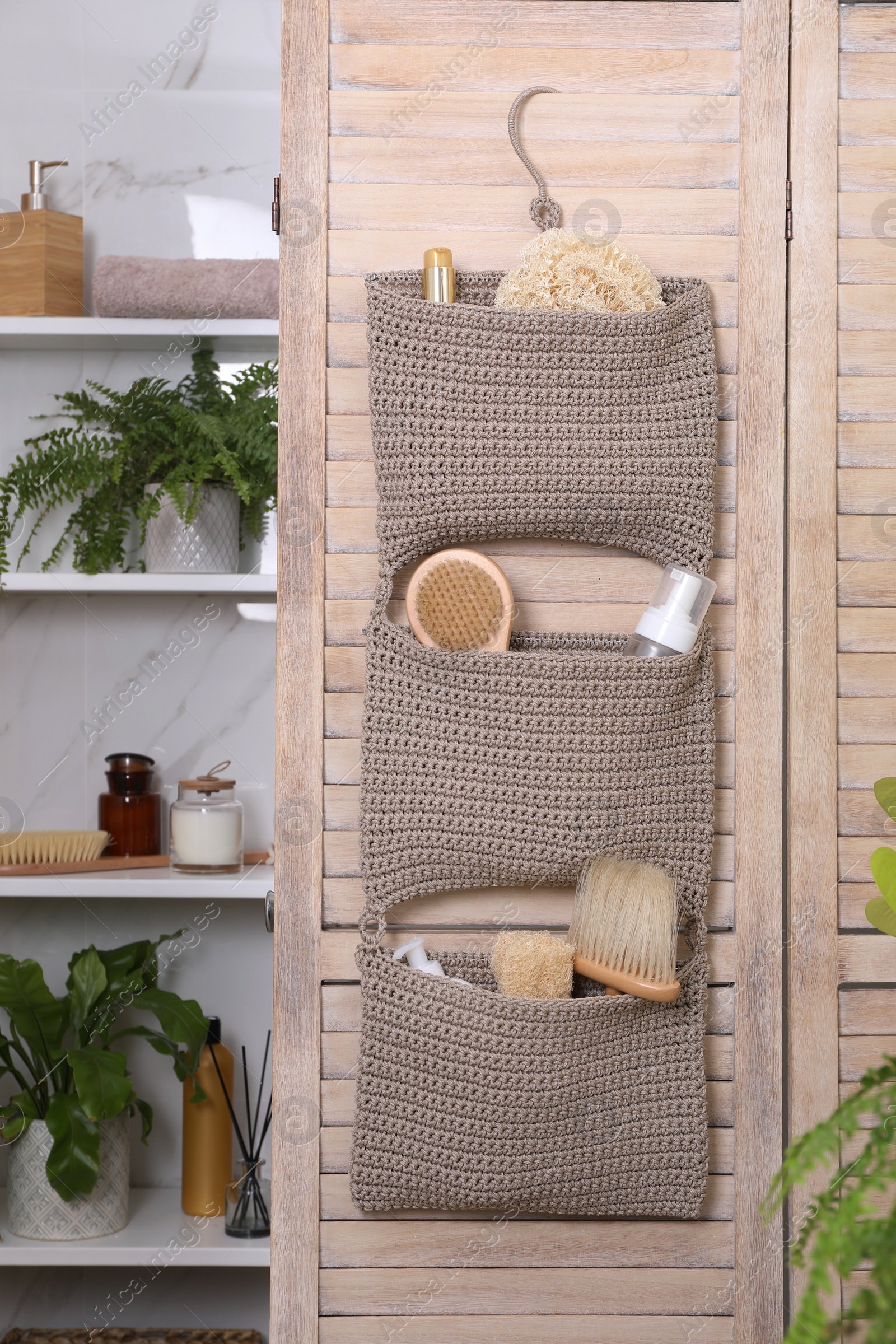 Photo of Storage with essentials hanging on wooden folding screen in bathroom. Stylish accessory