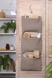 Photo of Storage with essentials hanging on wooden folding screen in bathroom. Stylish accessory