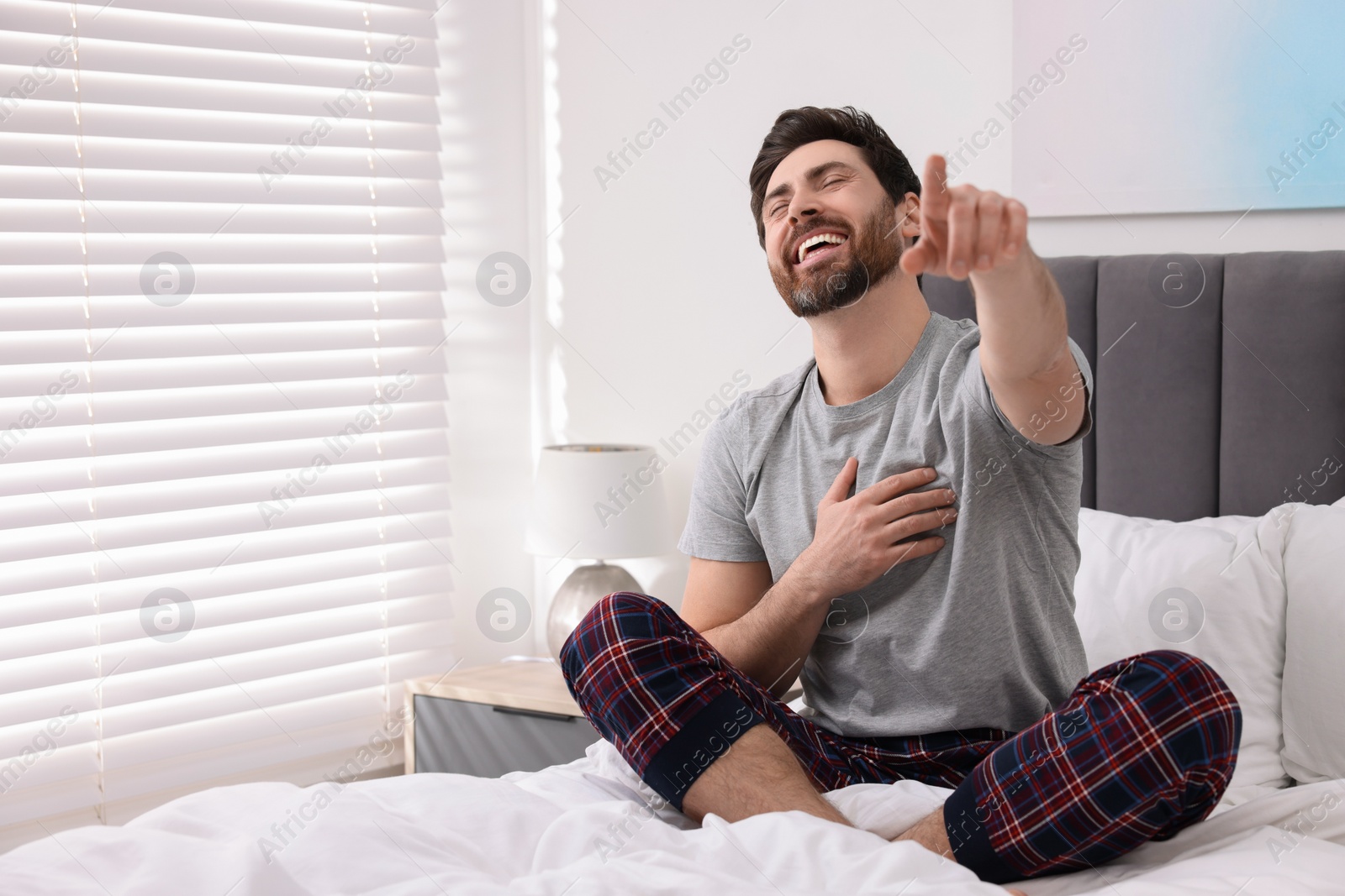 Photo of Handsome man pointing at something and laughing in bedroom. Space for text