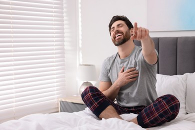 Photo of Handsome man pointing at something and laughing in bedroom. Space for text