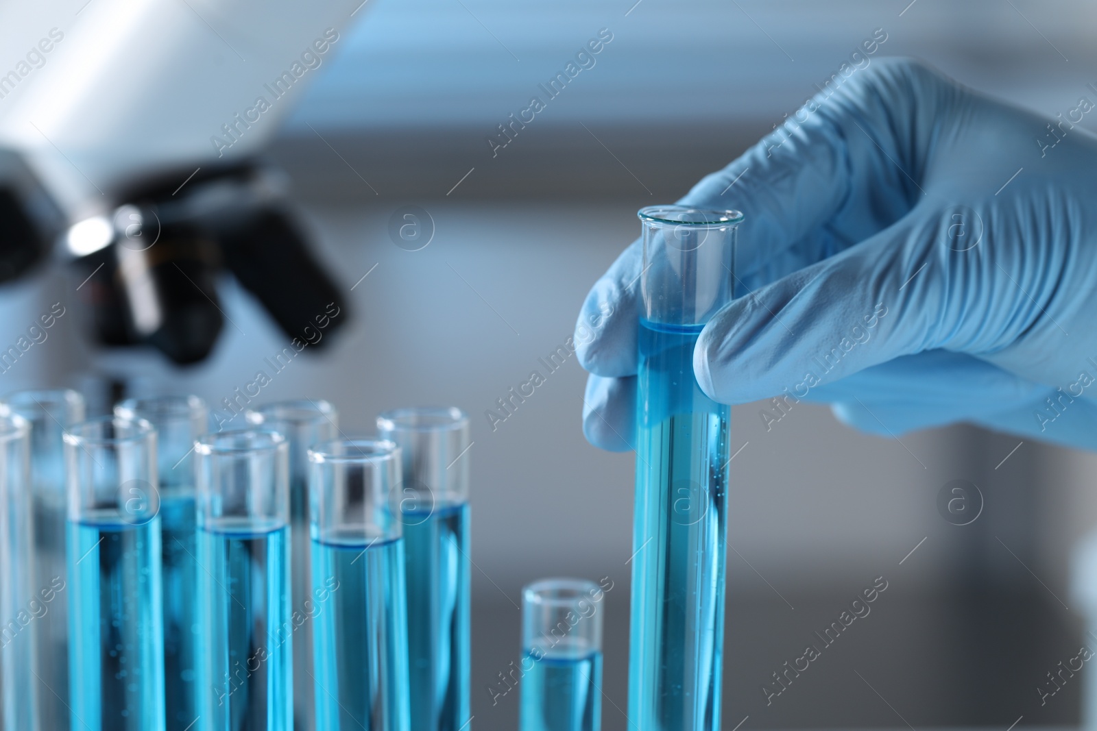 Photo of Scientist taking test tube with light blue liquid in laboratory, closeup. Space for text