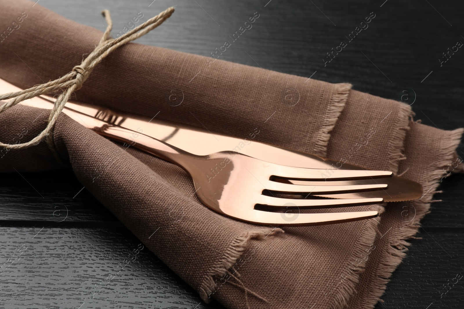 Photo of Stylish setting with cutlery and napkin on black wooden table, closeup