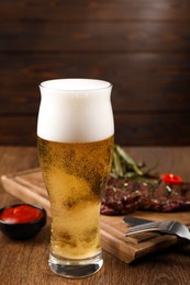 Glass of beer, delicious fried steak and sauce on wooden table