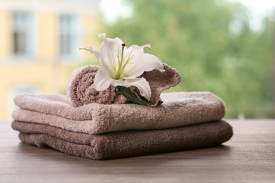 Photo of Pile of fresh towels and flower on wooden table against blurred background, space for text