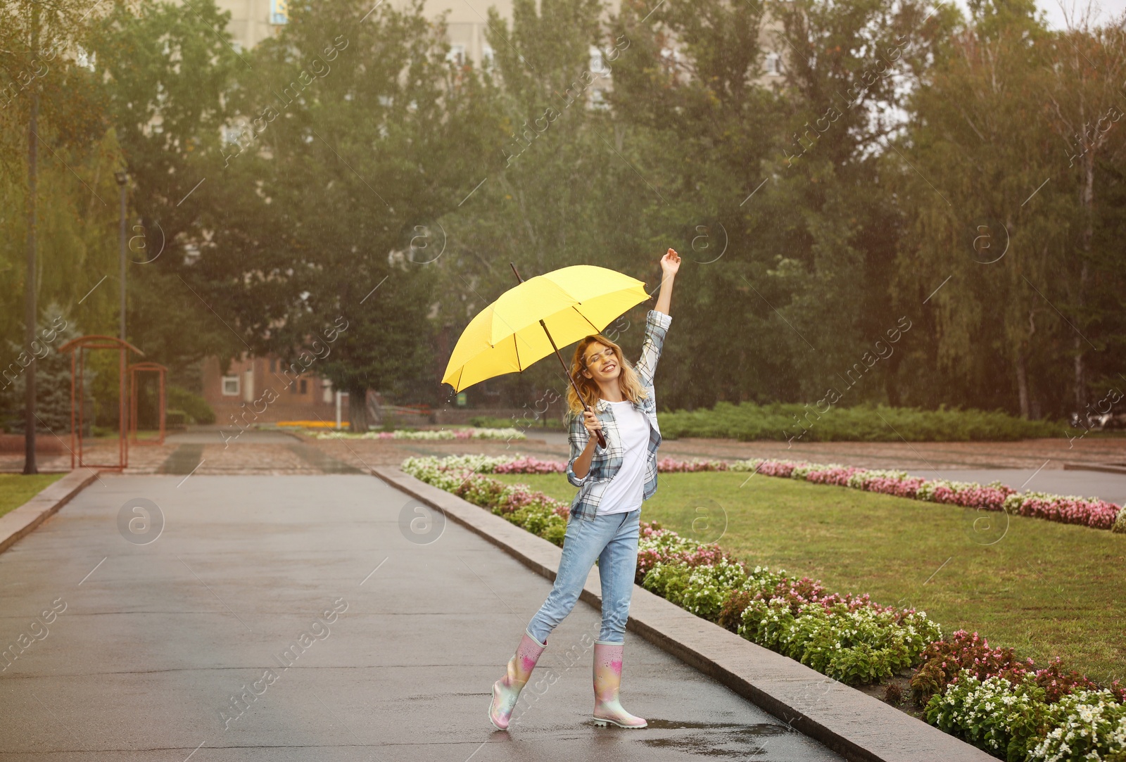 Photo of Happy young woman with umbrella under rain in park