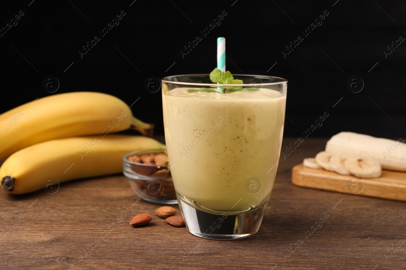 Photo of Glass with banana smoothie and mint on wooden table against black background