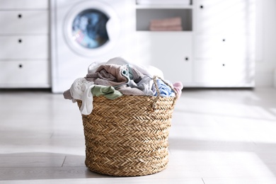 Photo of Wicker basket with dirty laundry on floor indoors